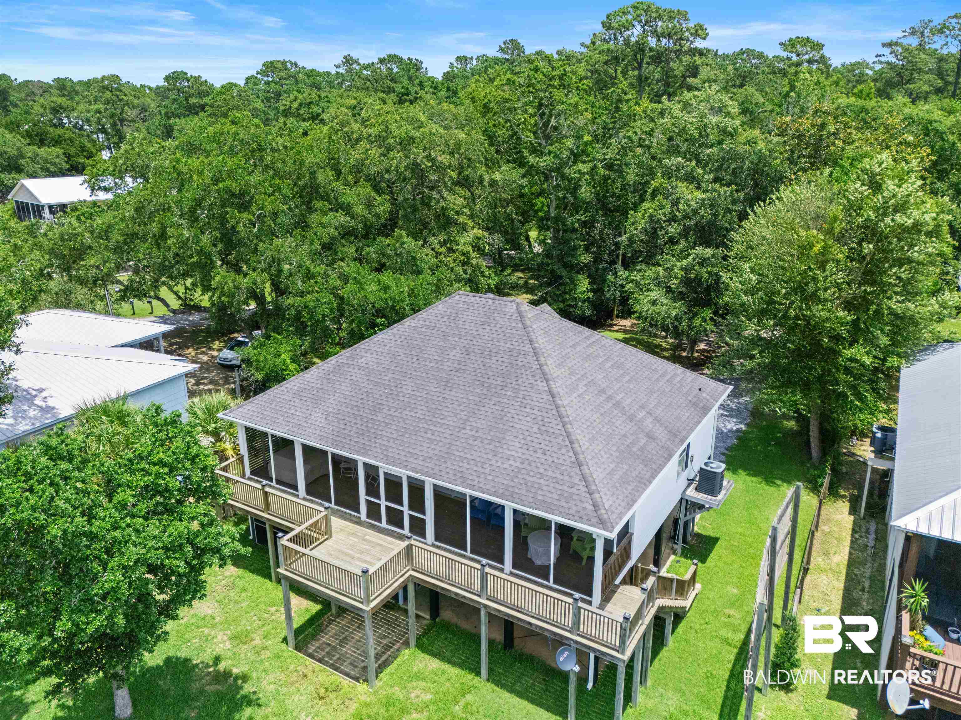 9581 South Bay Street Foley, AL 36535 - Photo 30 of 44 Elevated residence featuring a screened porch, multiple outdoor decks, a gray shingle roof, and a surrounding treeline