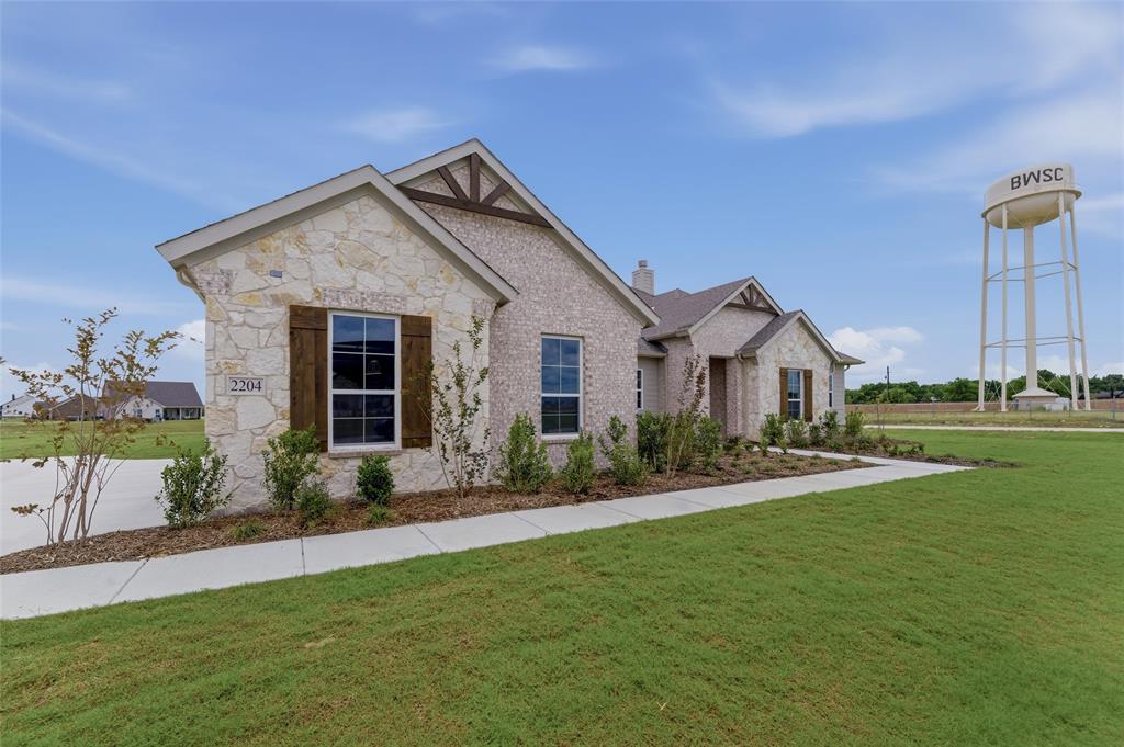 2204 Continent Court Krum, TX 76249 - Photo 2 of 28 Stone and brick exterior featuring wooden decorative shutters, a concrete walkway, mature landscaping, and an expansive green lawn