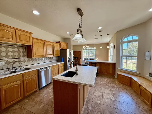 a large kitchen with stainless steel appliances a large counter top a sink a window and cabinets