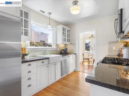 a kitchen with stainless steel appliances granite countertop a stove a sink dishwasher and white cabinets with wooden floor