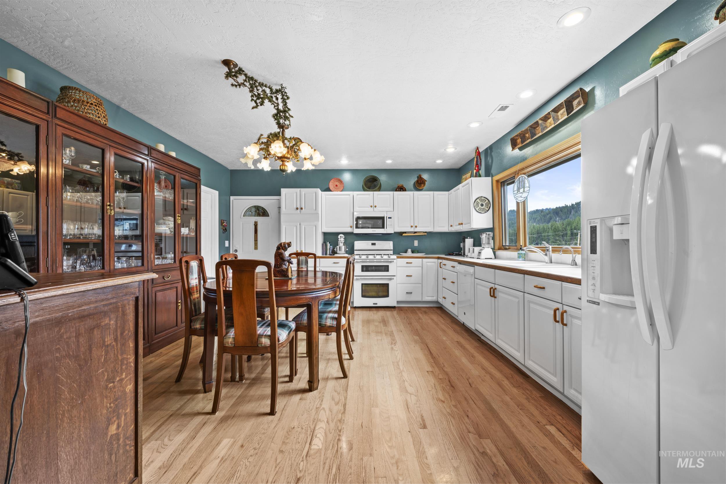 69 River Ranch Road Garden Valley, ID 83622 - Photo 12 of 50 Kitchen featuring white appliances, white cabinetry, a chandelier, light wood finished floors, and light countertops