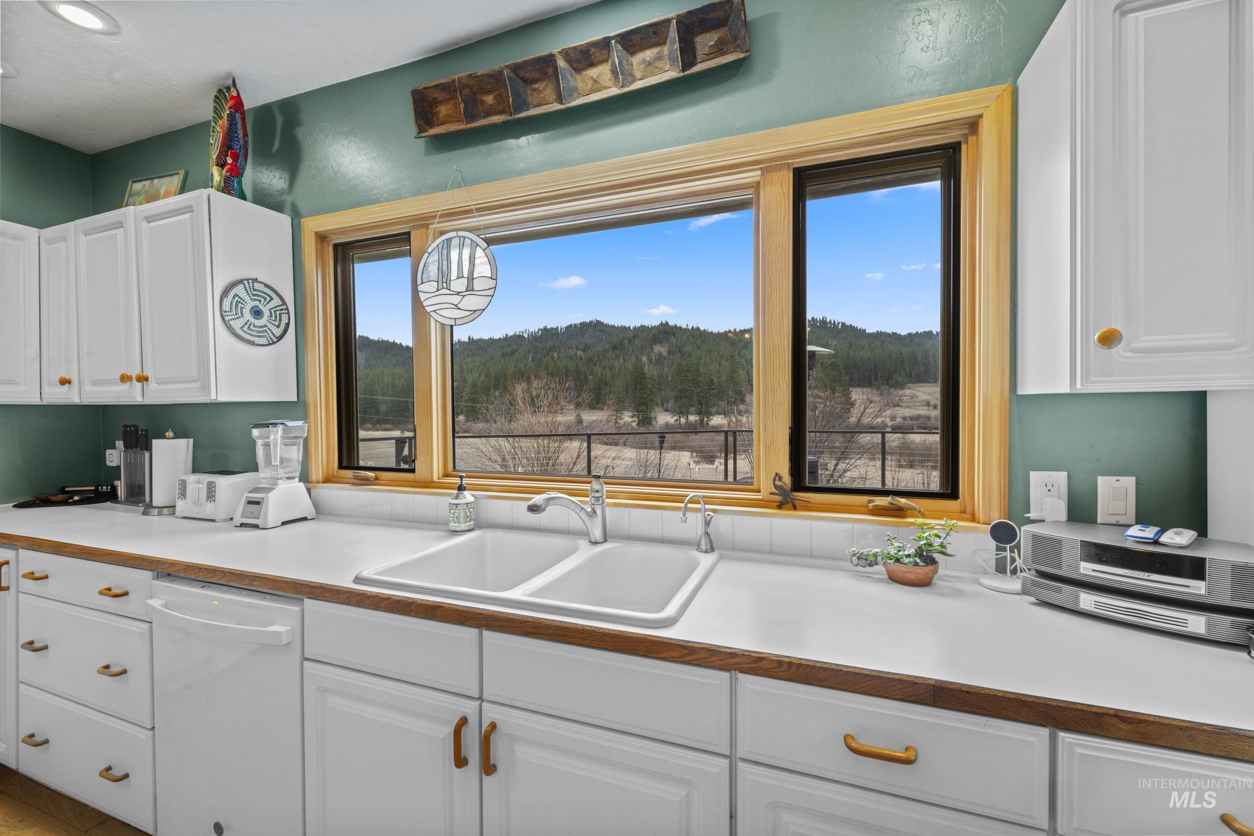 69 River Ranch Road Garden Valley, ID 83622 - Photo 14 of 50 Kitchen featuring white cabinetry, white dishwasher, light countertops, and a wooded view