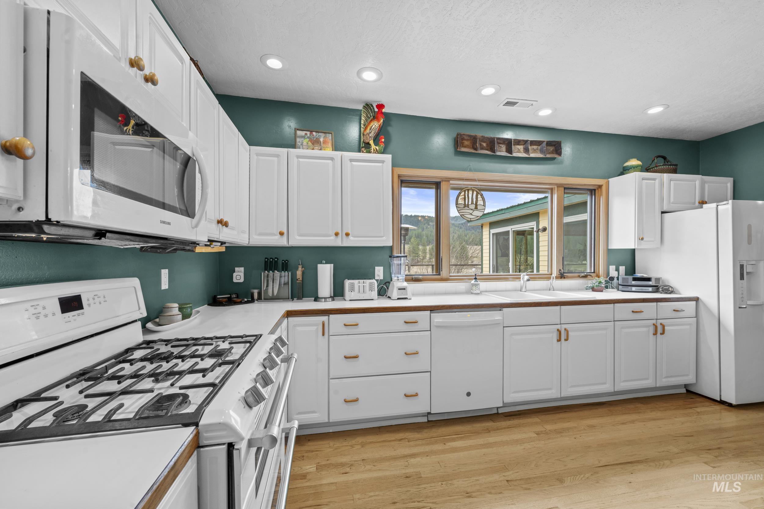69 River Ranch Road Garden Valley, ID 83622 - Photo 16 of 50 Kitchen featuring white appliances, white cabinetry, light countertops, light wood-style floors, and recessed lighting