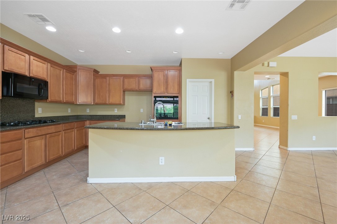 2289 Manosque Lane Henderson, NV 89044 - Photo 10 of 35 Kitchen featuring brown cabinets, recessed lighting, light tile patterned floors, dark stone counters, and black appliances