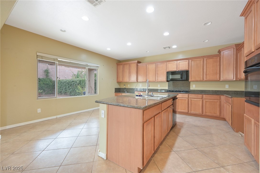 2289 Manosque Lane Henderson, NV 89044 - Photo 11 of 35 Kitchen with light tile patterned flooring, a center island with sink, recessed lighting, dark stone countertops, and black appliances