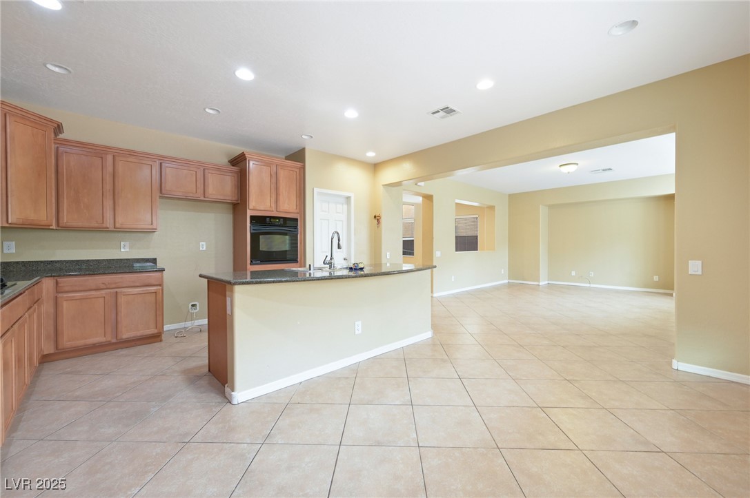 2289 Manosque Lane Henderson, NV 89044 - Photo 13 of 35 Kitchen with recessed lighting, light tile patterned floors, black oven, dark stone counters, and an island with sink