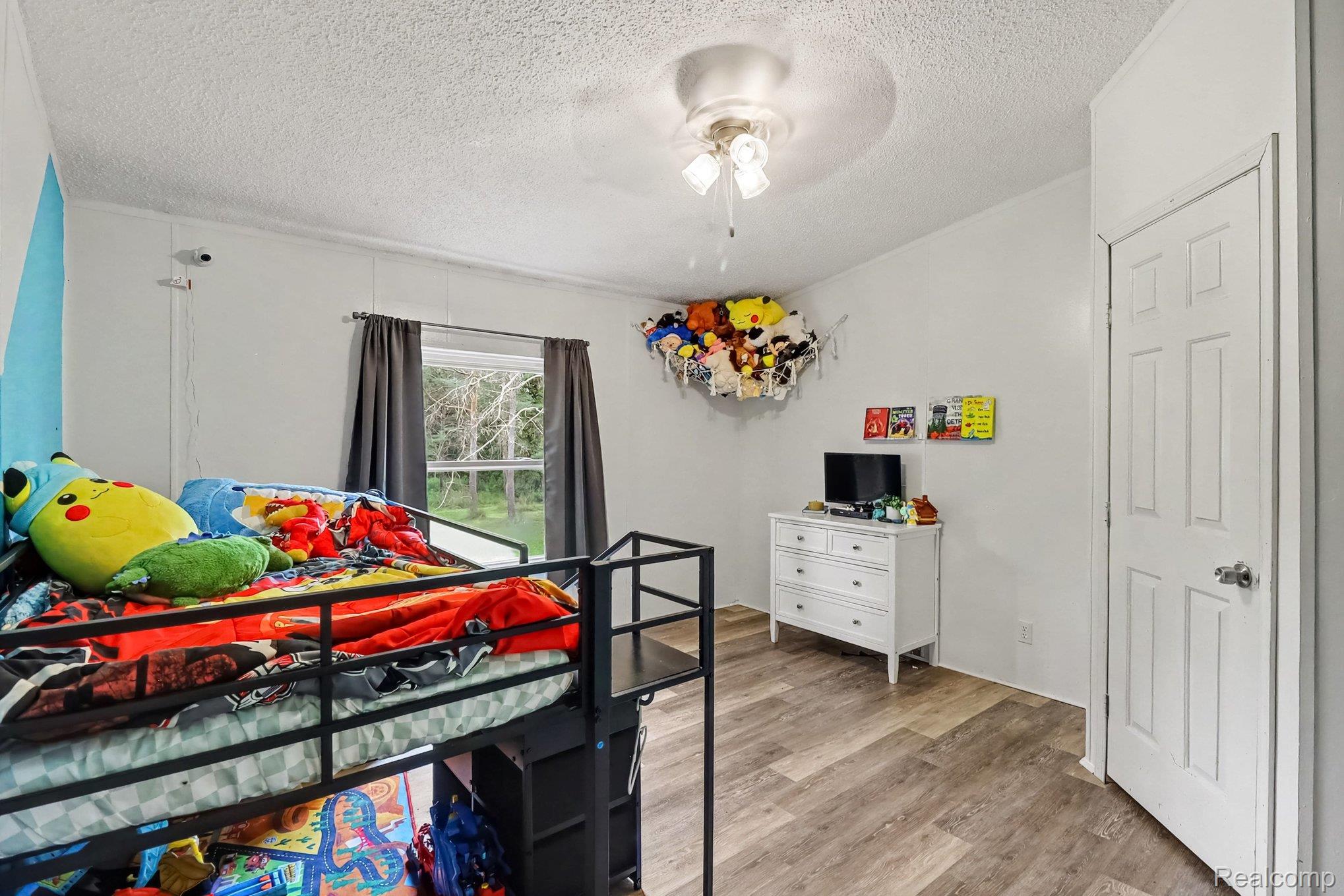 6357 North State Road Davison, MI 48423 - Photo 23 of 33 Bright secondary bedroom featuring wood-finish flooring, a black metal bed frame, white six-drawer dresser with integrated storage, large window with natural light, and ceiling-mounted light fixture