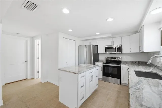 a large white kitchen with stainless steel appliances granite countertop a stove a sink a refrigerator and white cabinets with wooden floor