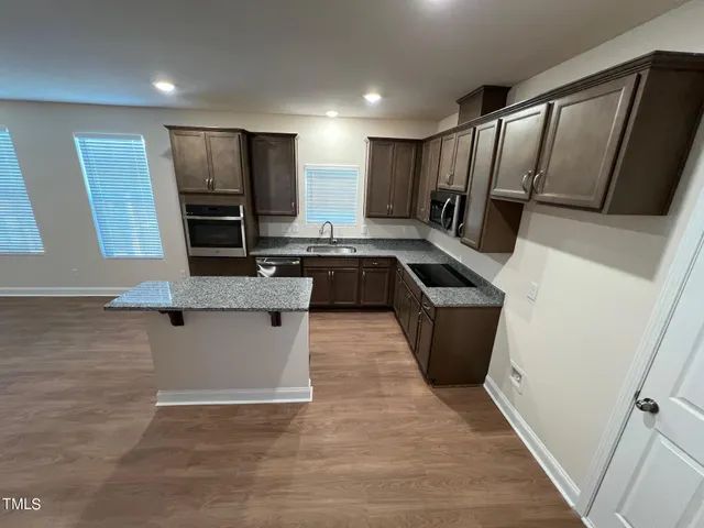 a kitchen with stainless steel appliances granite countertop a sink a stove a refrigerator a microwave oven with white cabinets and wooden floor