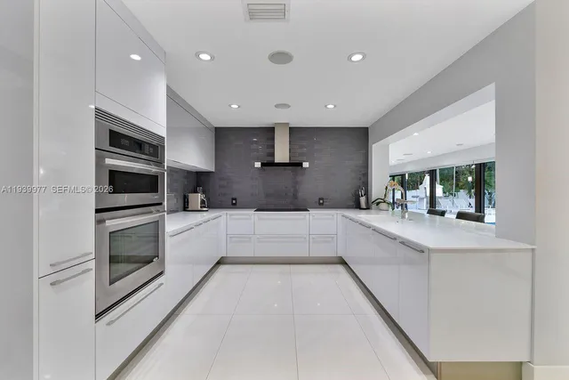 a large white kitchen with stainless steel appliances kitchen island a large counter top a stove a microwave and a refrigerator