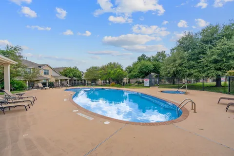 a view of a swimming pool with lawn chairs and large trees