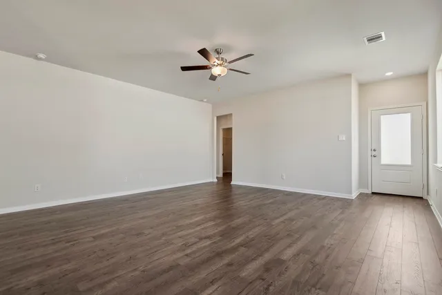 a view of an empty room with wooden floor and a ceiling fan
