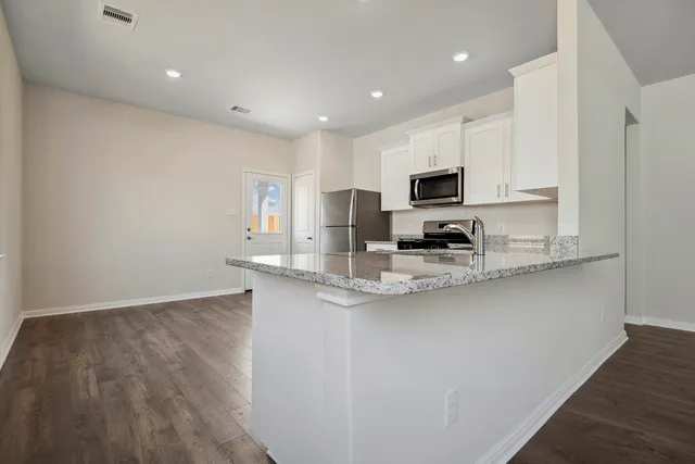 a kitchen with stainless steel appliances granite countertop a stove a sink a refrigerator and white cabinets