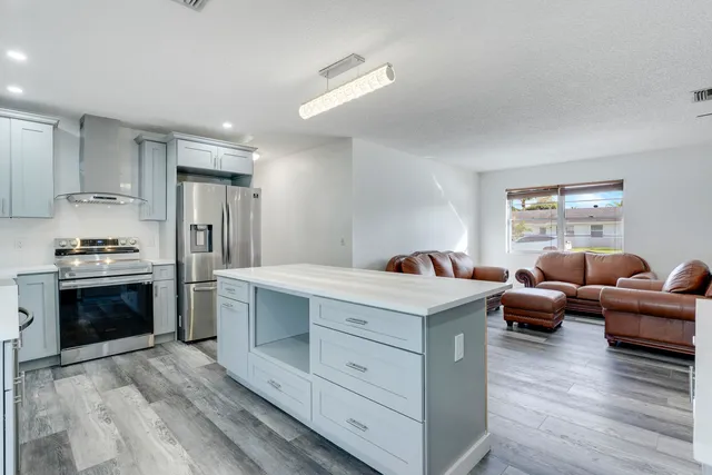 a living room with stainless steel appliances kitchen island granite countertop a stove a sink dishwasher a refrigerator and a dining table with wooden floor