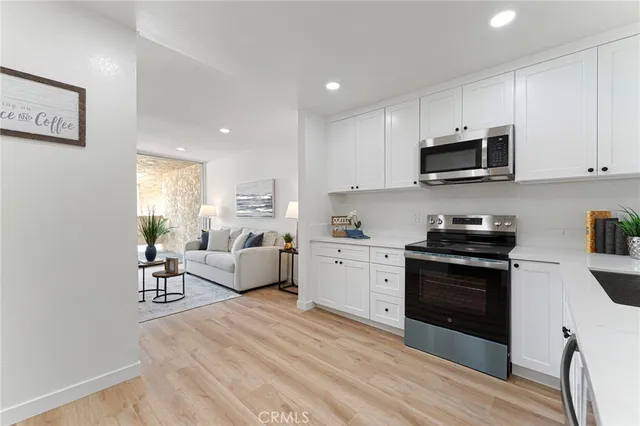 a kitchen with stainless steel appliances granite countertop a stove top oven a sink a refrigerator white cabinets and couches with wooden floor