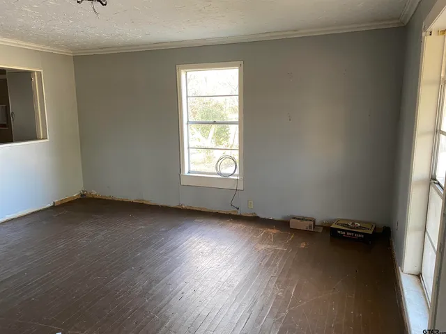 an empty room with wooden floor and windows with curtains