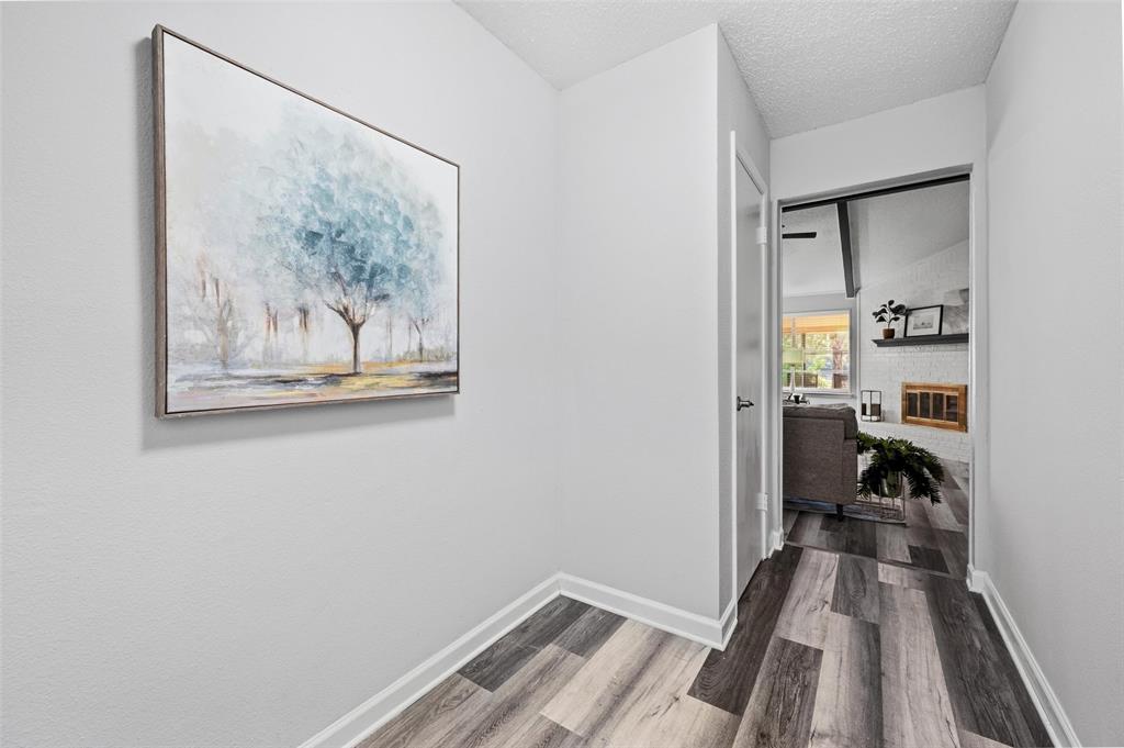 608 Ridgewood Circle Hurst, TX 76054 - Photo 6 of 38 Wood-finish flooring with white trim, leading to an interior doorway with a black door handle, revealing a white brick fireplace with a wood mantel