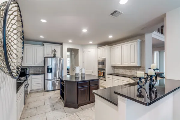 a room with stainless steel appliances kitchen island granite countertop a sink refrigerator and cabinets