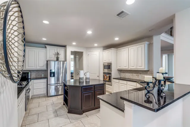 a room with stainless steel appliances kitchen island granite countertop a sink refrigerator and cabinets