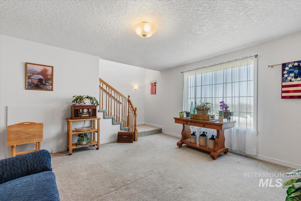 2331 Gulley Road Homedale, ID 83628 - Photo 17 of 46 Carpeted living area featuring a large window with sheers, a wooden staircase with balusters, and a ceiling-mounted light fixture