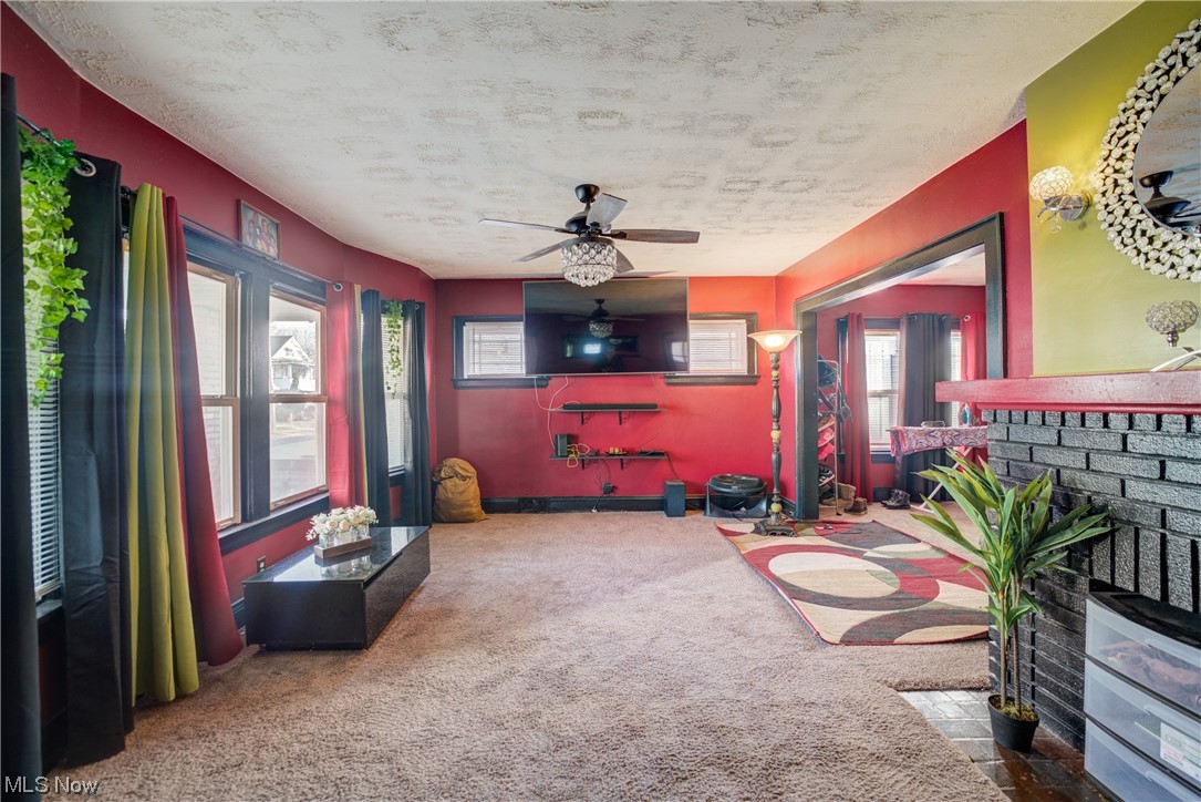 14202 Glenside Road Cleveland, OH 44110 - Photo 25 of 41 Living room featuring a textured ceiling, ceiling fan, a fireplace, and carpet floors