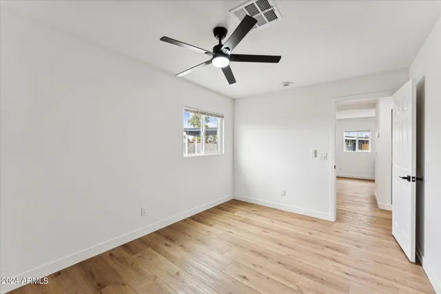 an empty room with wooden floor ceiling fan and windows