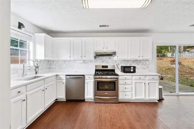 a kitchen with stainless steel appliances white cabinets a sink a stove a refrigerator and white cabinets
