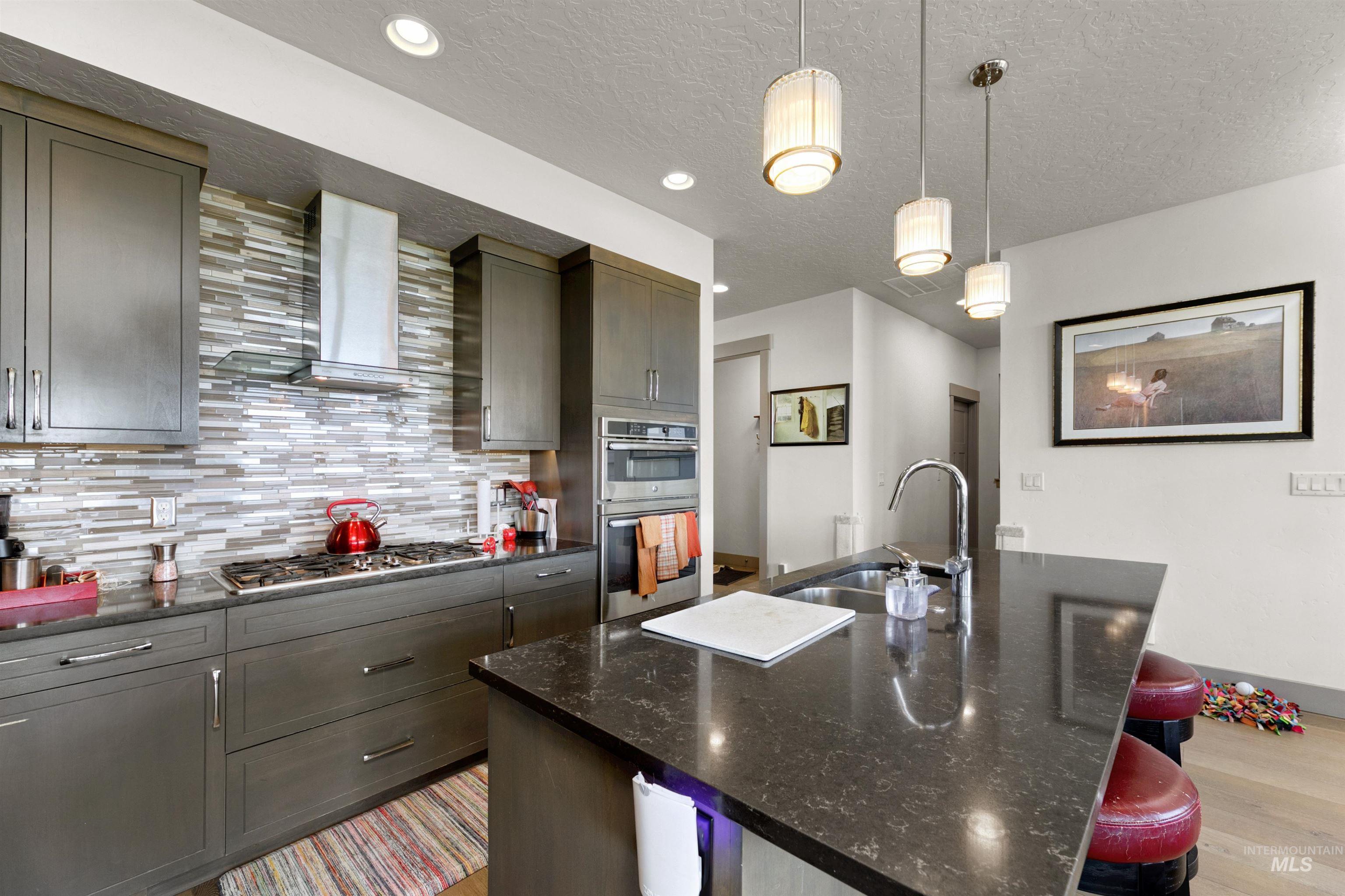 24398 Tombstone Ridge Court Middleton, ID 83644 - Photo 23 of 47 Modern kitchen featuring dark-stained cabinetry, a multi-tone horizontal tile backsplash, and dark countertops