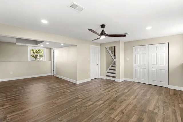 a view of an empty room with wooden floor and a ceiling fan