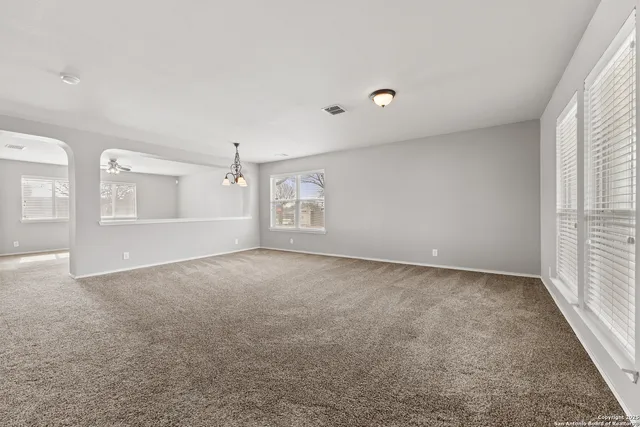 an empty room with windows and chandelier fan