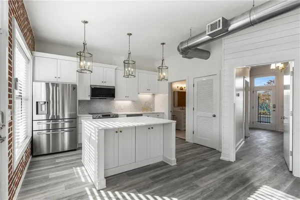a kitchen with stainless steel appliances kitchen island granite countertop a refrigerator a oven and white cabinets with wooden floor