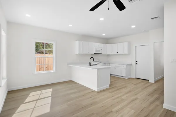 a large white kitchen with kitchen island a sink wooden floor and a refrigerator