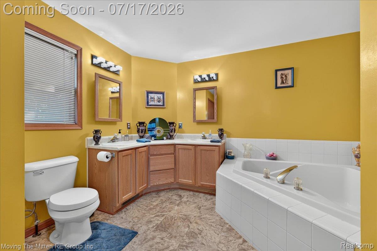 40162 Alden Road Belleville, MI 48111 - Photo 19 of 67 Bathroom featuring a corner soaking tub with white tile surround, a dual vanity with light wood cabinetry and integrated sinks, and a white toilet