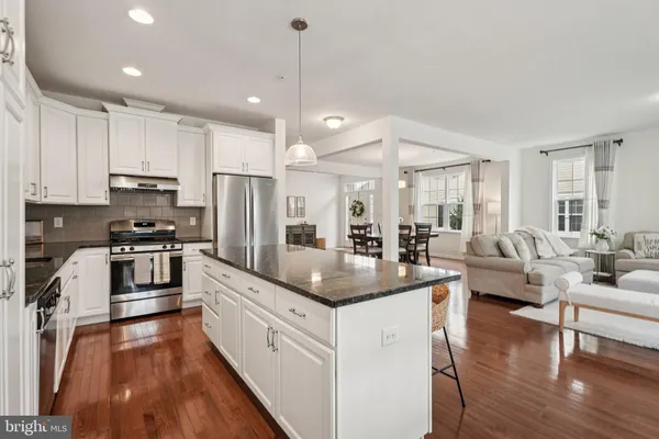 a kitchen with granite countertop a refrigerator a stove a sink and white cabinets with wooden floor