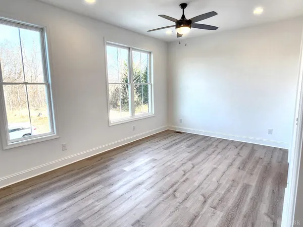 an empty room with wooden floor fan and windows