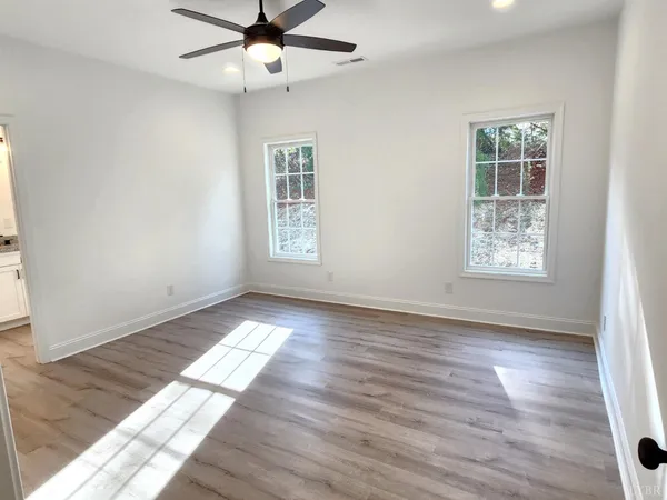 an empty room with wooden floor chandelier fan and windows