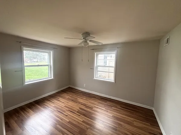 a view of an empty room with wooden floor and a window