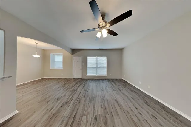 an empty room with wooden floor chandelier fan and windows
