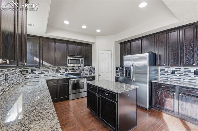 2224 Reed Grass Way Colorado Springs, CO 80915 - Photo 19 of 39 Kitchen featuring stainless steel appliances, a center island, light stone countertops, dark brown cabinetry, and dark wood-style floors