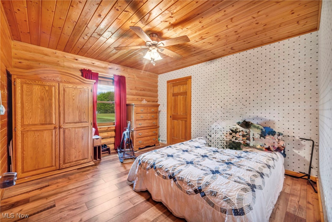 15180 Stoltz Road Diamond, OH 44412 - Photo 21 of 48 Main floorBedroom featuring wooden ceiling, light wood finished floors, wallpapered walls, ceiling fan, and log walls