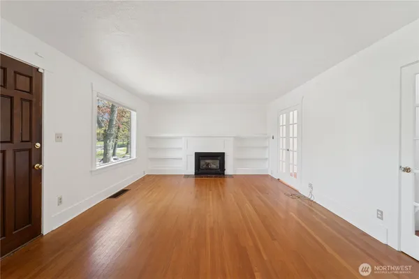 an empty room with wooden floor fireplace and windows