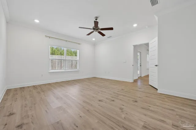 an empty room with wooden floor ceiling fan and windows