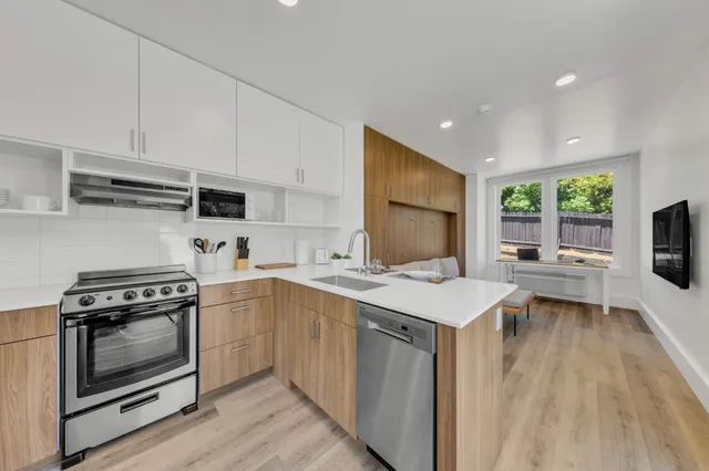 a kitchen with stainless steel appliances a refrigerator a sink a stove and white cabinets with wooden floor