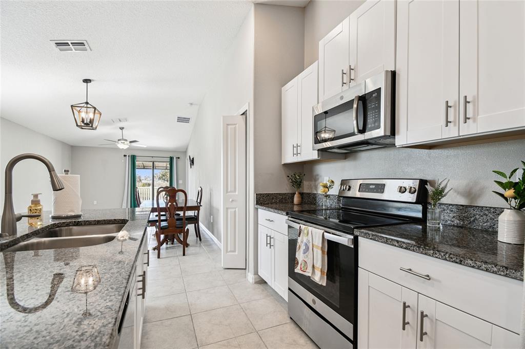 1735 Ripple Jade Place Ruskin, FL 33570 - Photo 12 of 68 a kitchen with stainless steel appliances granite countertop a stove top oven a sink a dining table and chairs with white cabinets