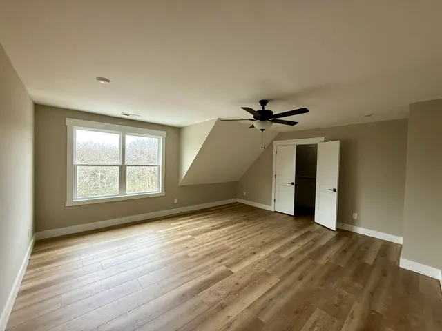 an empty room with wooden floor ceiling fan and windows