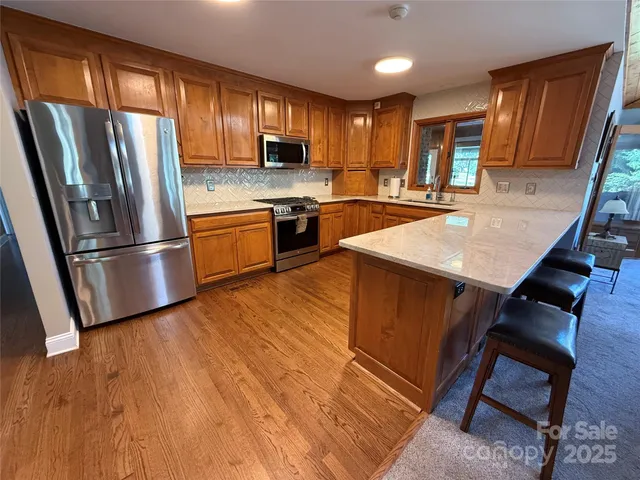 a kitchen with stainless steel appliances granite countertop a refrigerator a sink dishwasher a stove and white countertops with wooden floor