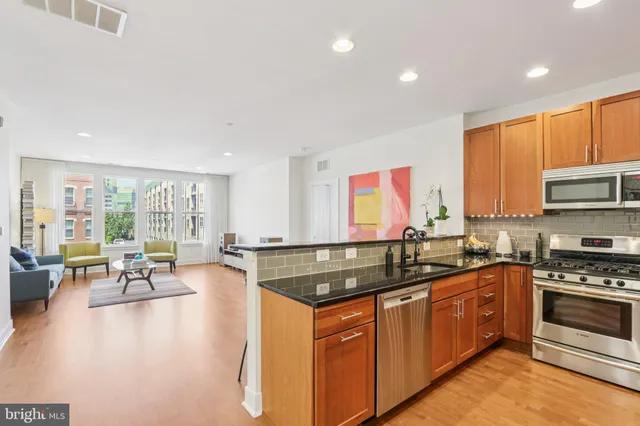 a kitchen with stainless steel appliances granite countertop a stove top oven a sink dishwasher a dining table and chairs with wooden floor