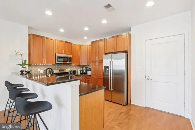 a kitchen with granite countertop a refrigerator a stove a sink a dining table and chairs with wooden floor