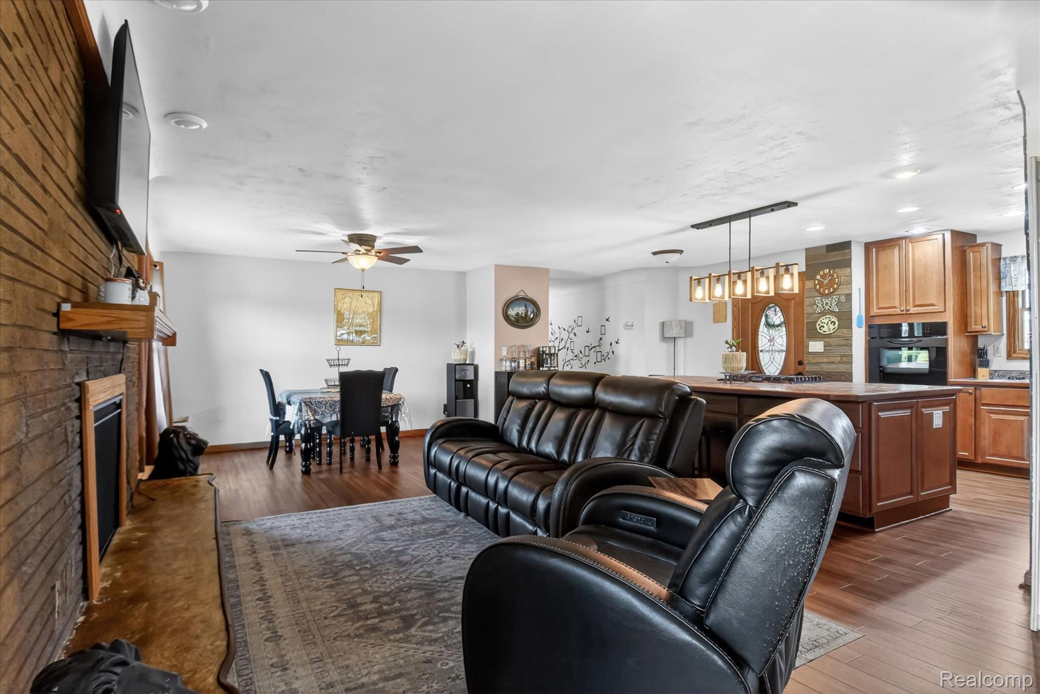 3949 West Burns Line Road Brown City, MI 48416 - Photo 14 of 70 Open-concept living space featuring wood-finish flooring, a brick-faced fireplace with a wood mantle, a dining area with a ceiling fan, and a kitchen island with pendant lighting
