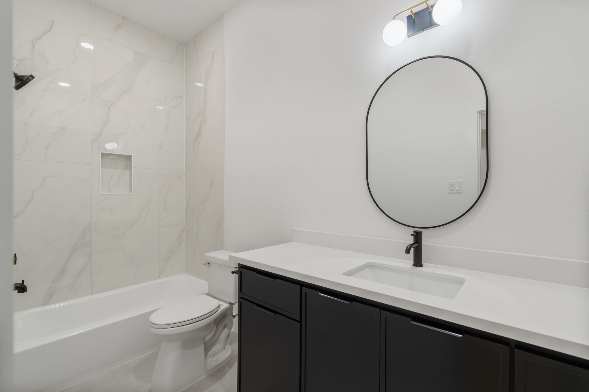 7321 Laura Koppe Road Houston, TX 77028 - Photo 32 of 41 Elegant bathroom featuring a sleek black
vanity, modern fixtures, and a stylish oval
mirror, complemented by a pristine white tub and
marble-patterned tiles for a contemporary feel.